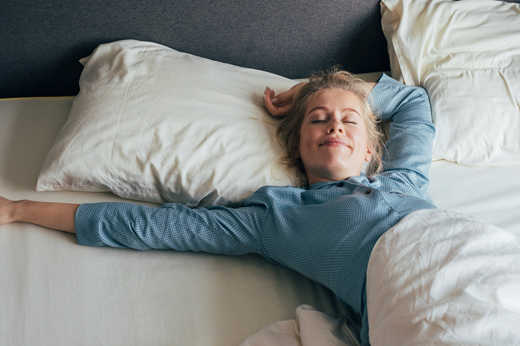Junge Frau wacht bequem und zufrieden in ihrem Bett auf.